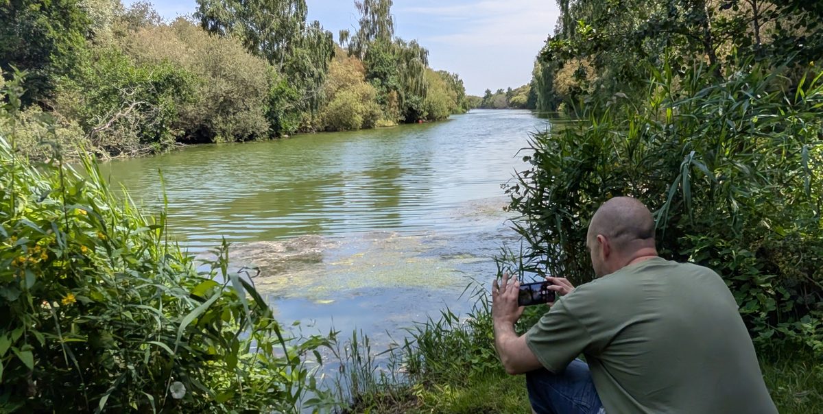 Elliott crouched on the bank at Westbere, taking a photo of the swim on his phone.